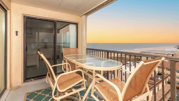 A balcony with a glass table and wicker chairs, overlooking a beach. - Ocean Front Condo with Pool (Ocean City)