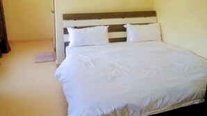 A single bed with white bedding in a room with plain walls and a wooden headboard. - FAVOURED HOTEL (Mwanza)
