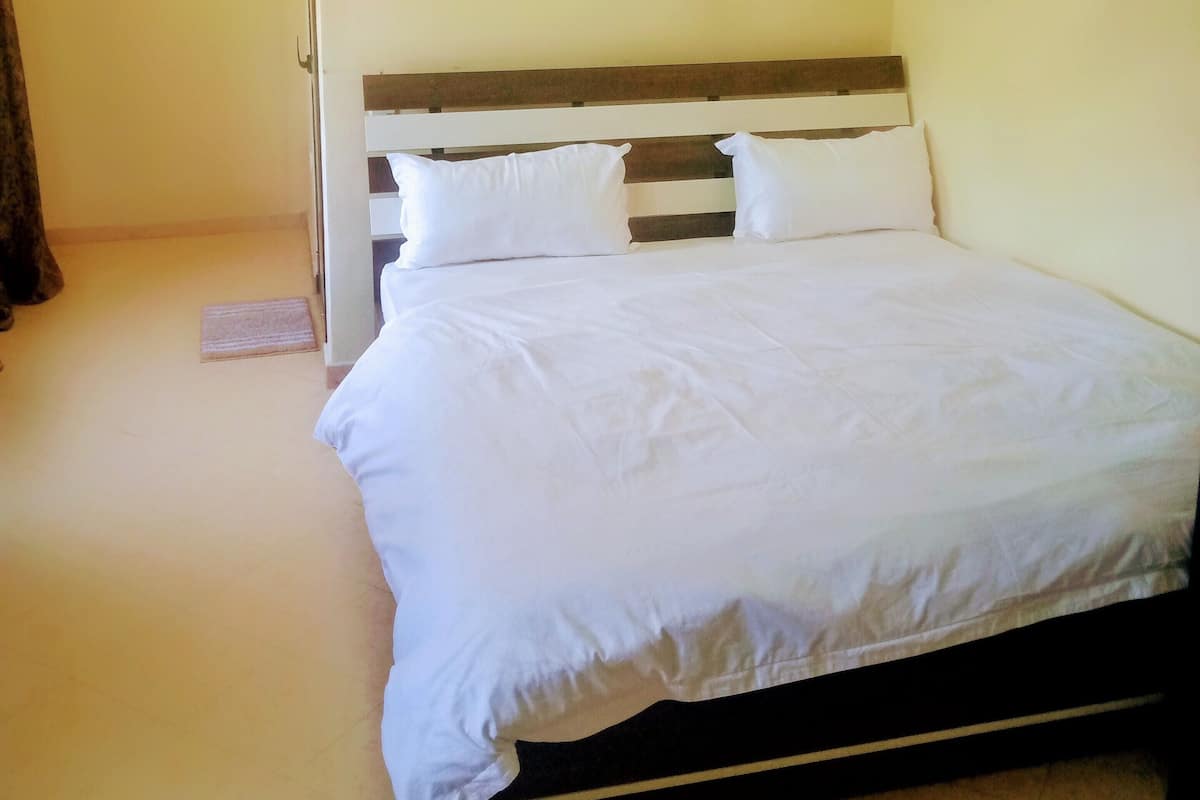 A single bed with white bedding in a room with plain walls and a wooden headboard.
