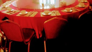 A round table with a red tablecloth, surrounded by red chairs, in a room with a window and an air conditioning unit. - FAVOURED HOTEL (Mwanza)