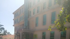 A multi-story building with a ground-level entrance and a balcony. Several white minibuses are parked in front. - FAVOURED HOTEL (Mwanza)