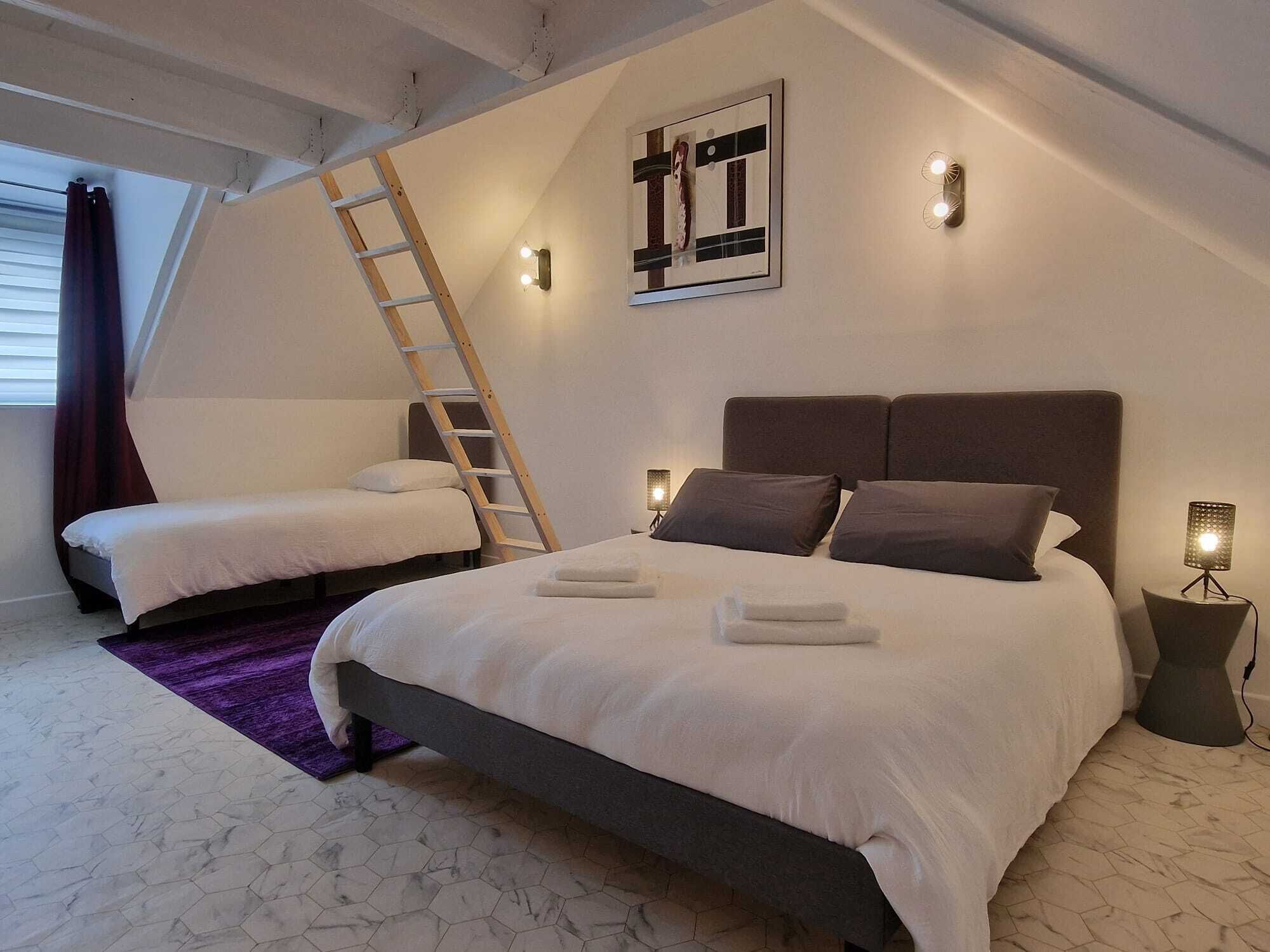 A bedroom with two beds, a ladder, a wall-mounted light, and a floor lamp.