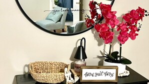 A black console table with a woven basket, a candle, a small sign, and a potted plant with red flowers. - Charming 3-bedroom house with WiFi and AC in beautiful Richmond (Richmond)