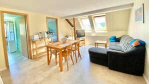 A spacious living area with a dining table, a sofa, and a TV. There are skylights and a view of the outdoors. - Vacations for Explorers in the Elbe Sandstone Mountains and Saxon Switzerland National Park (Sebnitz)