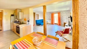 A modern kitchen with a dining area, a blue sofa, and a brick wall. - Vacations for Explorers in the Elbe Sandstone Mountains and Saxon Switzerland National Park (Sebnitz)