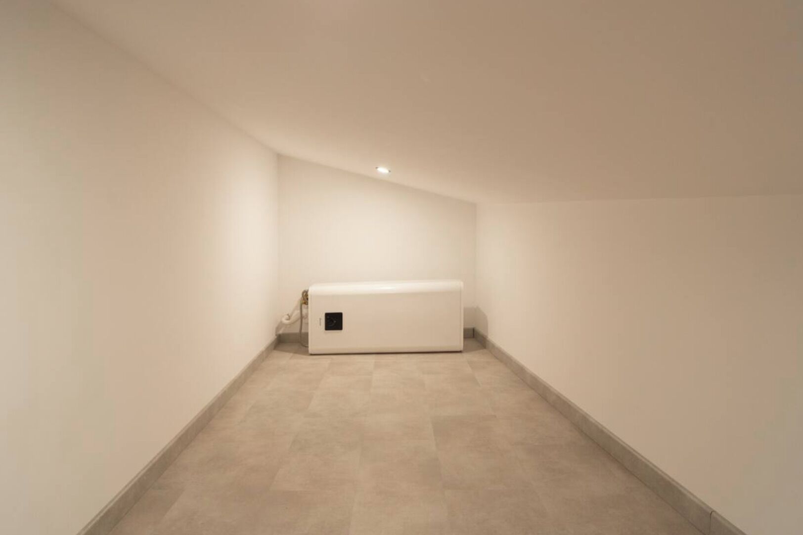 Un couloir étroit et vide, avec un radiateur blanc et un sol carrelé.