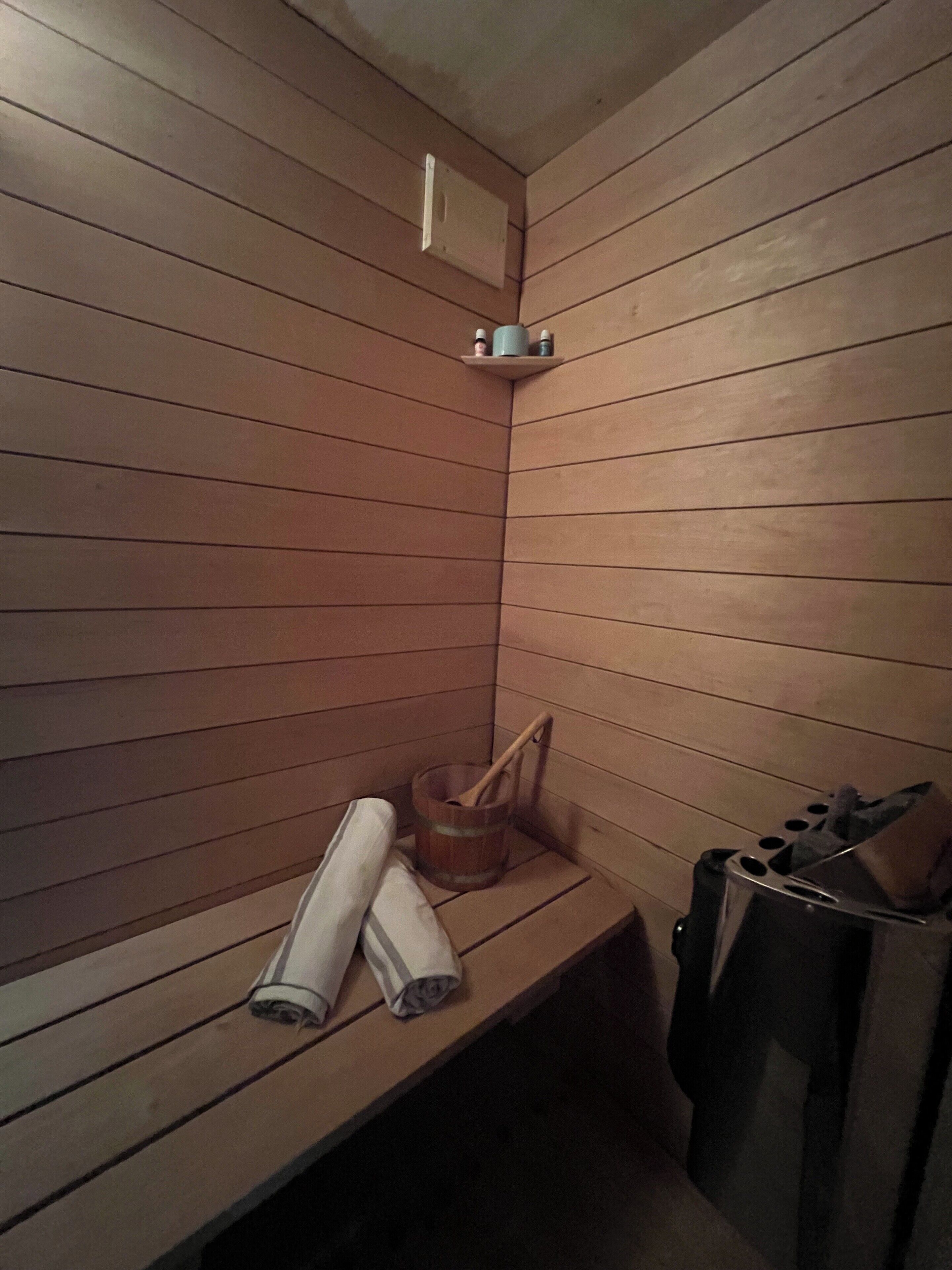 Un cuarto de sauna con bancos de madera, un balde de madera y un cubo de basura.