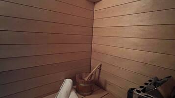 Un cuarto de sauna con bancos de madera, un balde de madera y un cubo de basura.