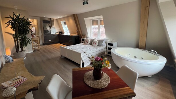 A bedroom with a large bed, a sitting area with a table and chairs, a bathroom with a bathtub, and a kitchen area. - Wellness-Loft: sauna, jacuzzi&  cinema. Centrally located near the station (Bodegraven)
