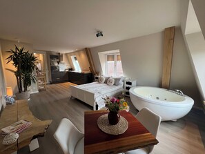 Une chambre avec un grand lit, un coin salon avec une table et des chaises, une salle de bain avec une baignoire et un coin cuisine.