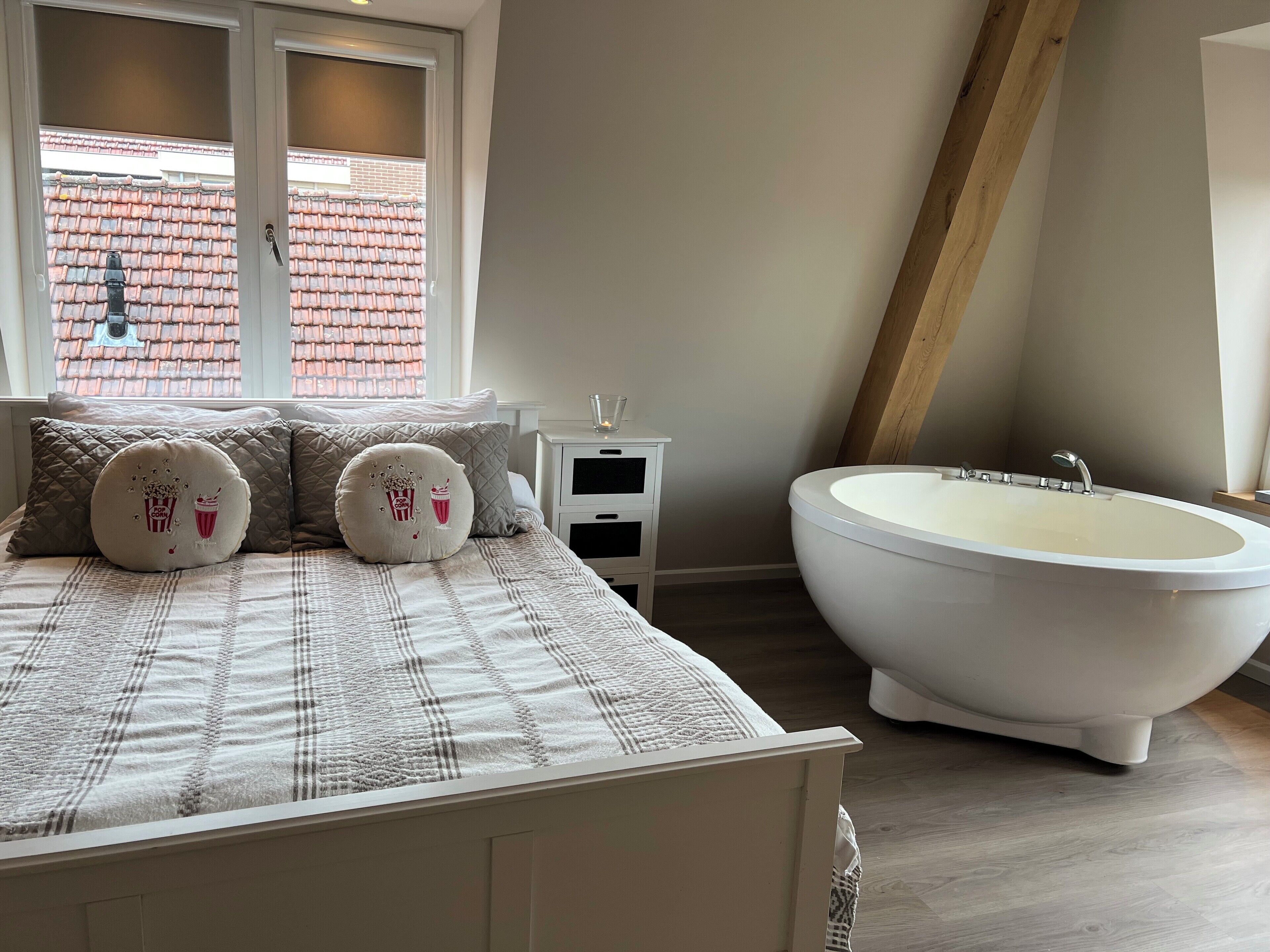 Une chambre avec un grand lit, une table de chevet blanche, un verre d’eau et une baignoire sur pieds.