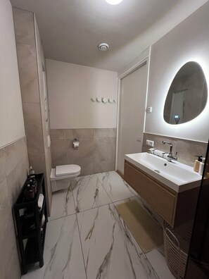 Une salle de bain moderne avec un sol en marbre, un lavabo blanc, un grand miroir et des toilettes.