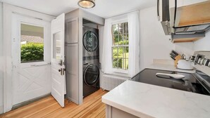A kitchen with a built-in oven, a window with curtains, and a view of greenery outside.