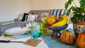 Une table à manger avec un verre à vin, des assiettes, un couteau, un saladier de fruits et une plante en pot.