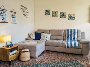 Uma sala de estar com sofá, almofadas, luminária, mesa pequena com luminária e obras de arte na parede.