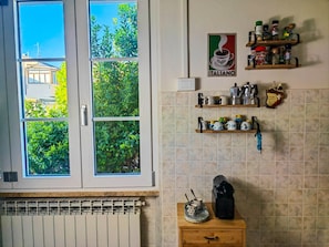 A kitchen with a window, a coffee machine, and shelves with kitchenware.