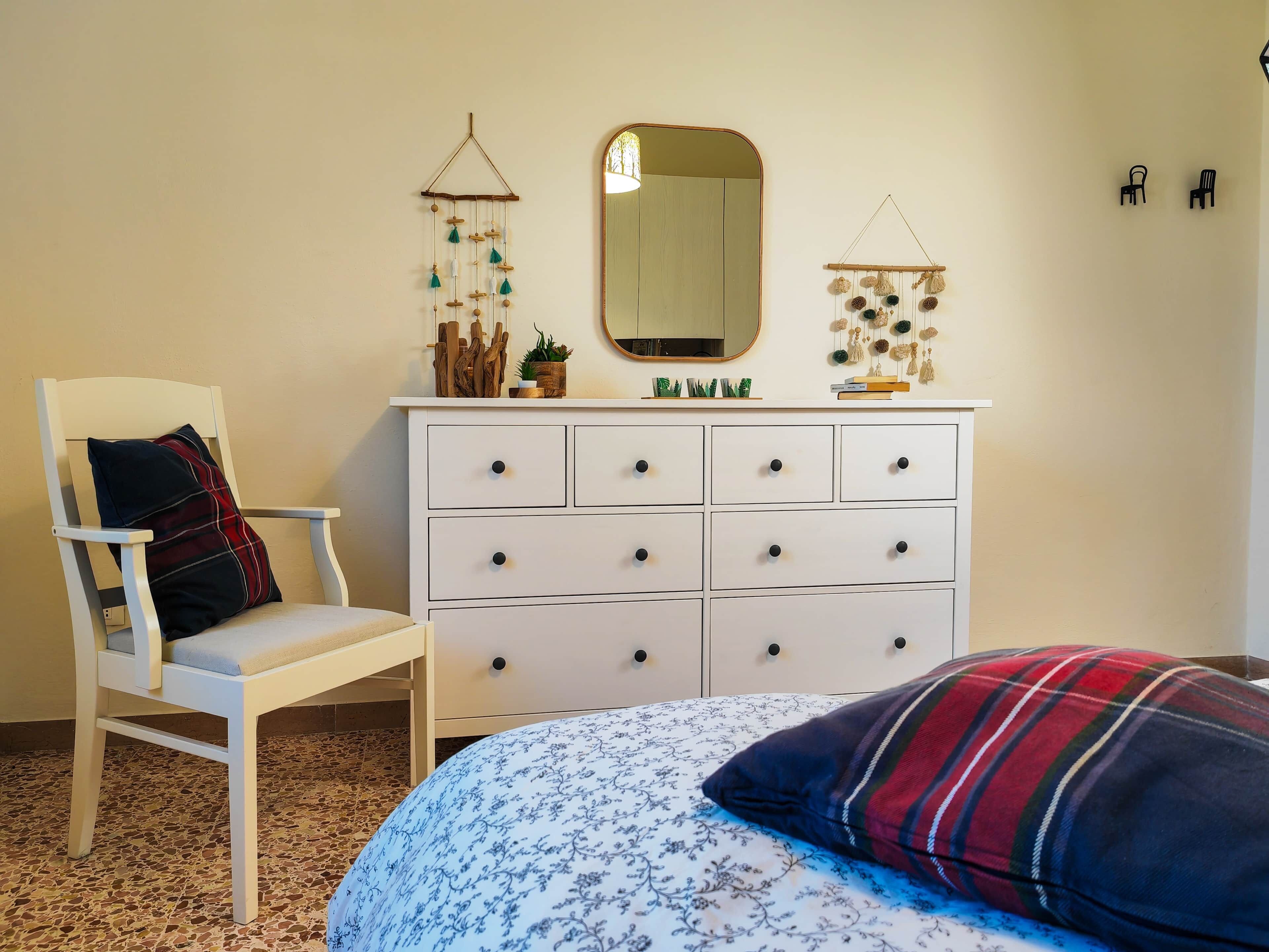 A bedroom with a bed, a chair, a dresser, a mirror, and wall decorations.