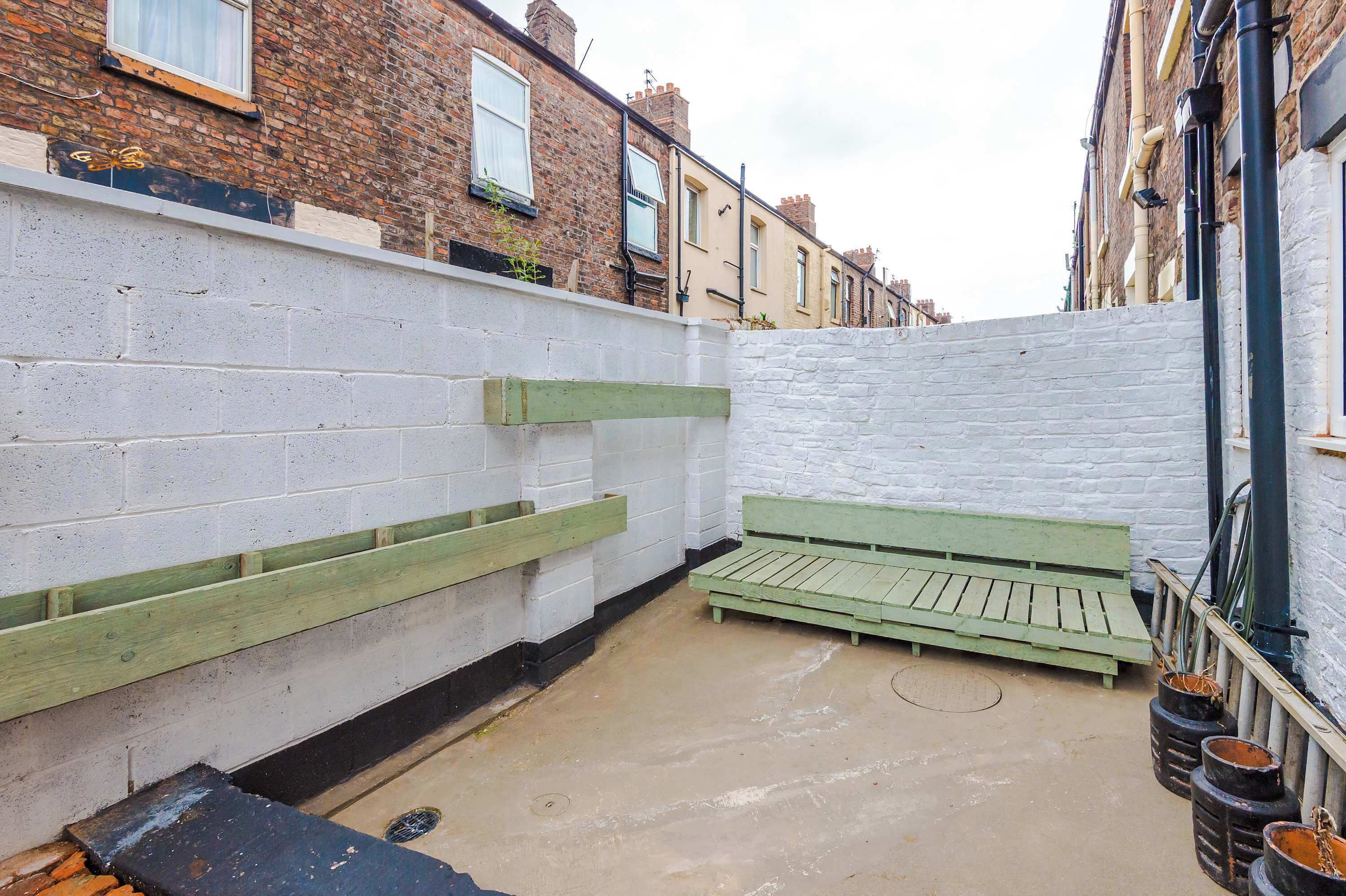 Une ruelle étroite avec un banc vert, des murs en briques blanches et une rangée de maisons mitoyennes.