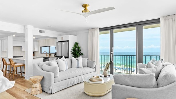 A modern living room with a sofa, a coffee table, and a dining area with chairs. There is a large window with a view of the ocean. - Rare Front Stack Remodeled 2 bedroom Gem in Mainsail- Free Beach Service! (Miramar Beach)