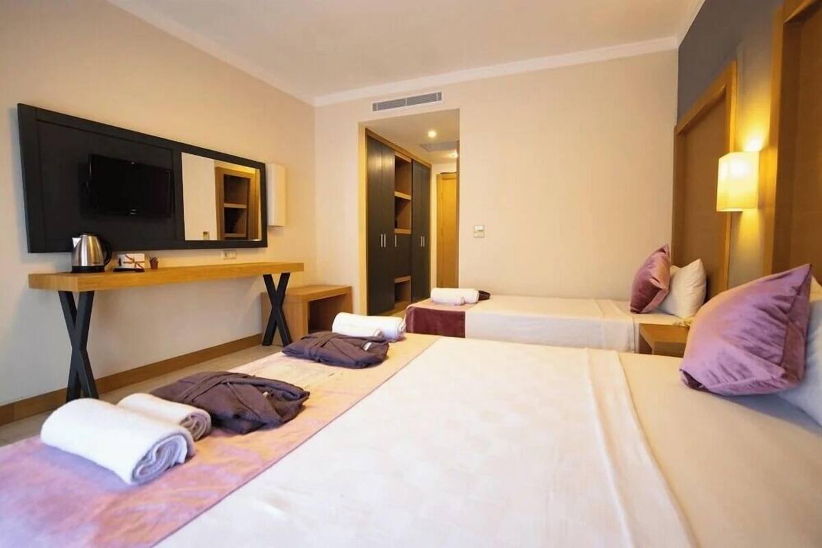 Una habitación de hotel con dos camas, televisión, escritorio y espejo.