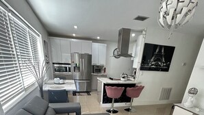Una sala moderna con un sofá modular, un comedor con mesa y sillas, una cocina con electrodomésticos de acero inoxidable, y un gran globo decorativo en el techo.