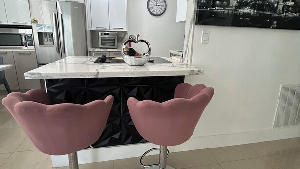 Cocina moderna con armarios blancos, electrodomésticos de acero inoxidable, una isla central con taburetes rosados, un reloj y una fotografía grande en blanco y negro de la Torre Eiffel en la pared.