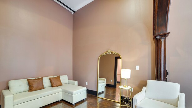 A room with a white sofa, a white armchair, a mirror, and a small table with a lamp. - Heart of Downtown Marshall: Boutique Studio Stay! (Marshall)