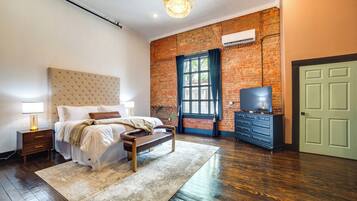 A bedroom with a large bed, a dresser, a television, and a brick wall.