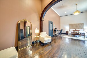 Una habitación amplia con un espejo grande, un sillón blanco, piso de madera y una cama con cabecera.