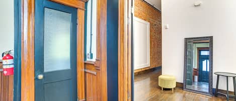 Un pasillo con suelo de madera, un extintor, un otoman amarillo y un espejo en la pared.