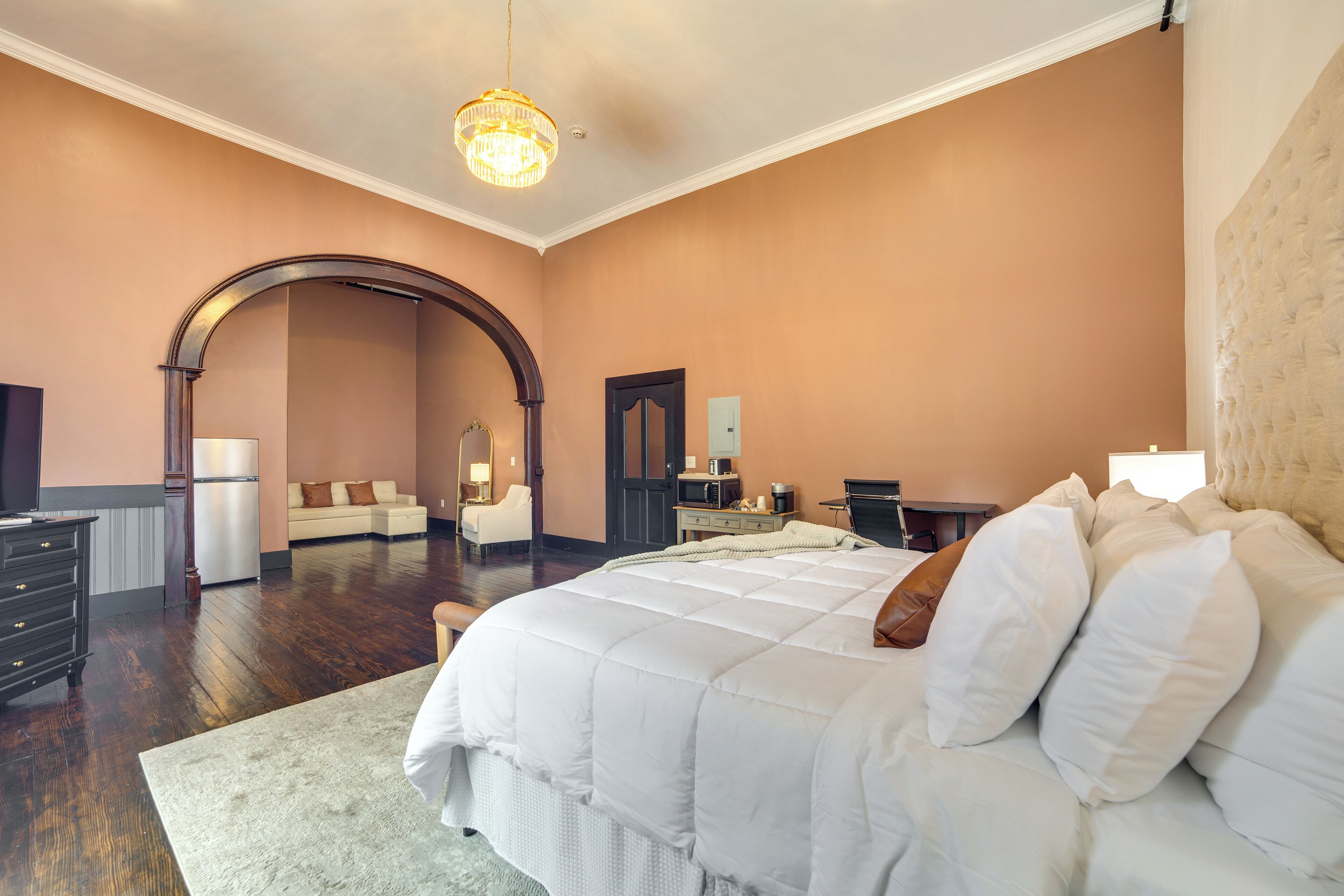 Un dormitorio amplio con una cama grande, piso de madera, una araña, un sofá y un rincón comedor.