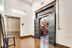 Un pasillo interior con un ascensor, una escalera y una puerta que da a otra habitación.