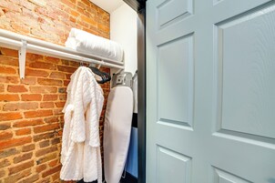 Habitación de hotel con pared de ladrillo, puerta blanca y un toallero con toallas y una plancha.