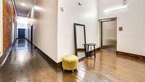 A hallway with wooden flooring, a yellow ottoman, a large mirror, and an elevator. - Heart of Downtown Marshall: Boutique Studio Stay! (Marshall)
