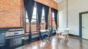 A modern kitchen with a stainless steel stove, a dining table with chairs, and large windows with black curtains. - Steps to Shops & Dining: Downtown Marshall Studio! (Marshall)