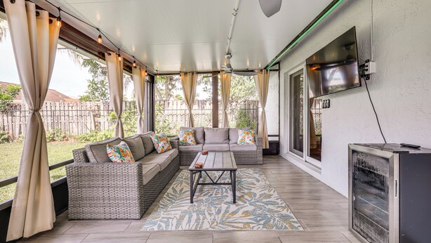 A covered outdoor seating area with a sofa, a table, and a TV mounted on the wall.