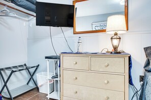 Een slaapkamer met een houten dressoir, een spiegel, een aan de muur bevestigde televisie en een lamp op het dressoir.