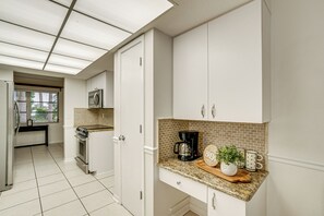 Una cocina moderna con armarios blancos, una encimera de granito, una cafetera y una ventana con vistas a árboles.