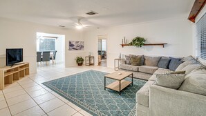 A spacious living room with a large sofa, a coffee table, and a TV on a wooden stand. There is a dining area in the background with a table and chairs. - 2 Mi to Beach: Home w/ Pool in Venice (Venice)
