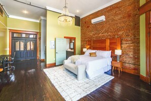 A bedroom with a brick wall, a wooden headboard, a white bed, and a nightstand with a lamp.