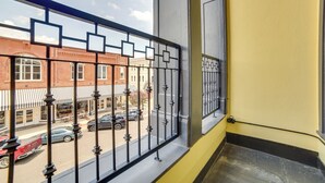 Ein Balkon mit Metallgeländer, der auf eine Straße mit parkenden Autos und Gebäuden blickt.