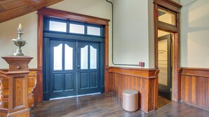 Ein Zimmer mit einer dunklen Holztür, einer kleinen runden Mülltonne und einer hölzernen Bank mit einer Lampe.