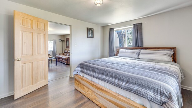A bedroom with a wooden bed, a large window with curtains, and a door leading to another room. - Secluded Stay: Serene Farmhouse in Trinidad! (Trinidad)