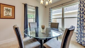 A dining area with a glass table, four chairs, a chandelier, and a framed picture on the wall.