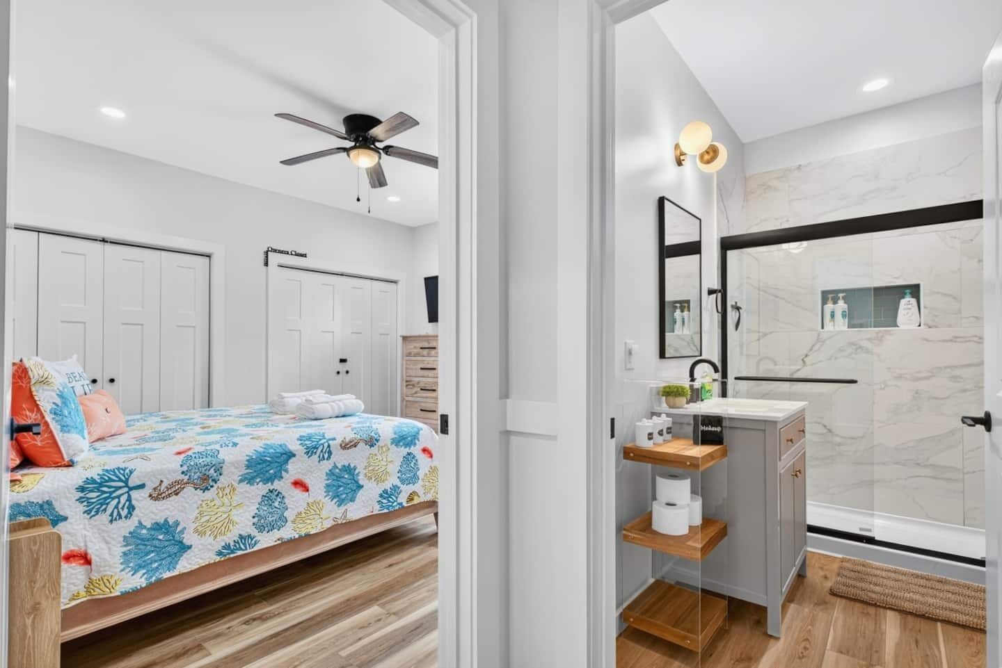Una camera da letto con un letto, un ventilatore a soffitto e un bagno dotato di lavandino, specchio e doccia.