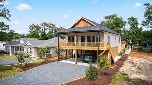 A two-story house with a covered porch and a small deck. - Lux Oak Island Retreat | Walk to Beach | Private Suite + Fenced Yard, Swim Spa Coming Soon! (Oak Island)