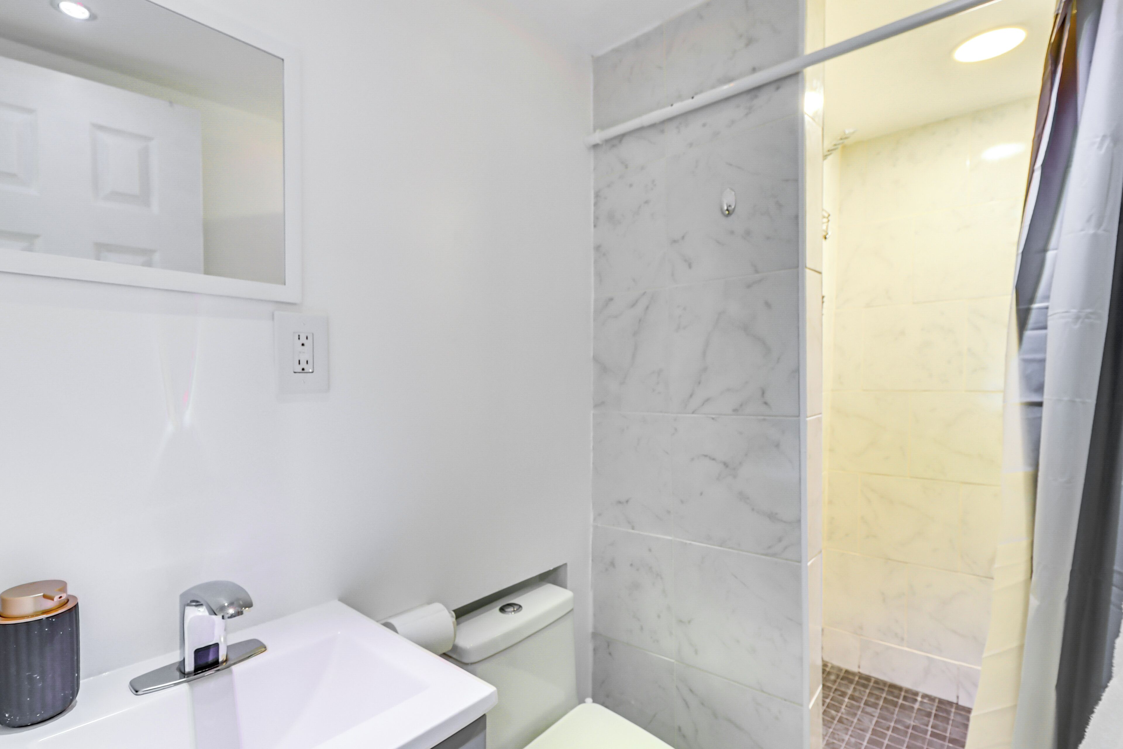 Een moderne badkamer met een wit wastafelmeubel, spiegel en betegelde douchewanden van marmer.