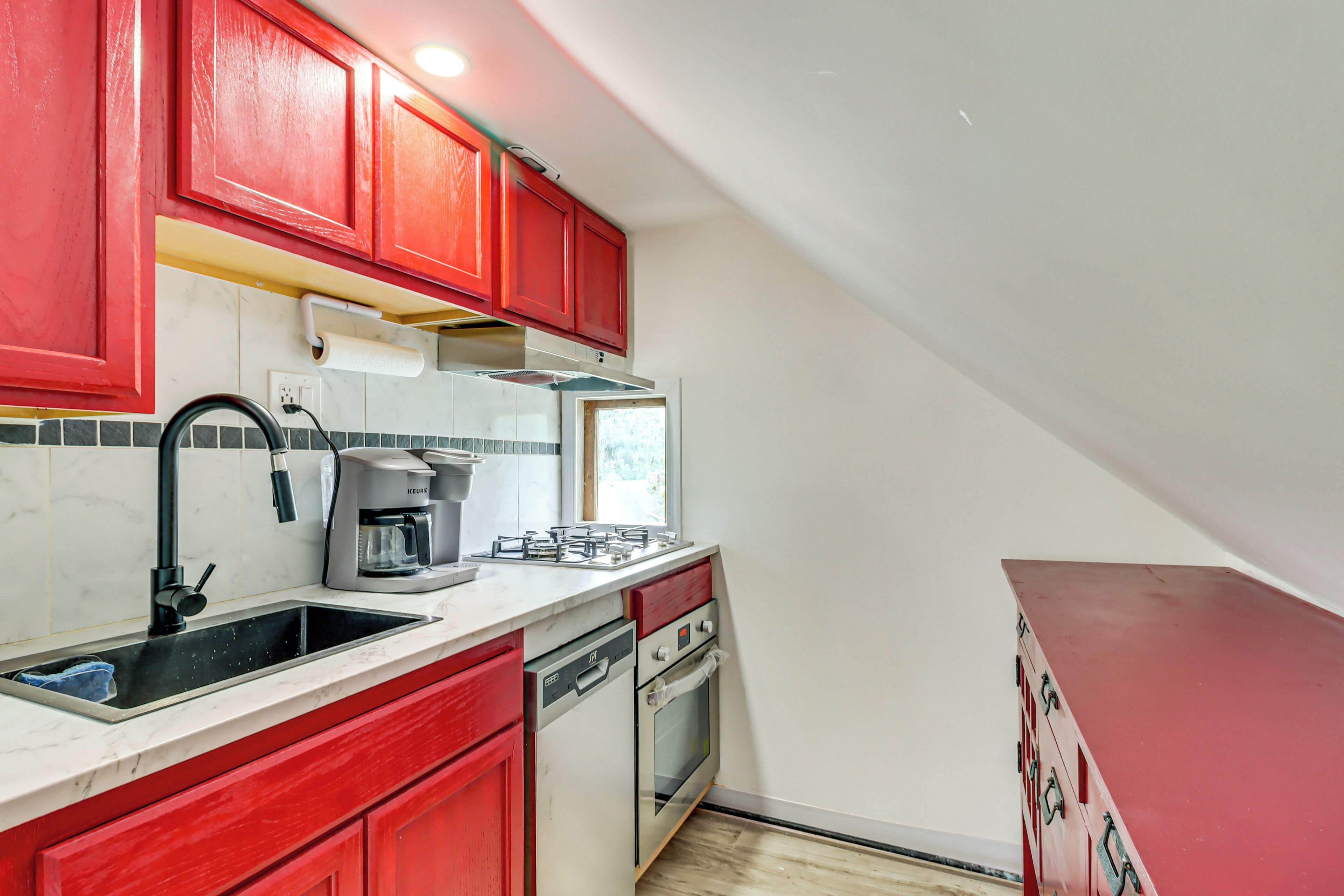 A kitchen with red cabinets, a white countertop, a coffee maker, a dishwasher, and an oven.