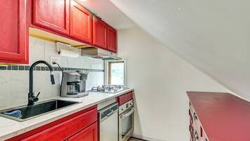 A kitchen with red cabinets, a white countertop, a coffee maker, a dishwasher, and an oven.