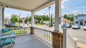 A porch with a white railing, green chairs, and a view of a street with cars and buildings. - Walk to Main St Stroudsburg! Pocono Townhome (Stroudsburg)